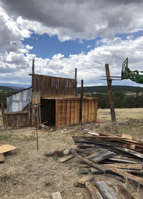 Chicken coop structure half-down — exposed frame, storm building behind, corrugated metal peeling away