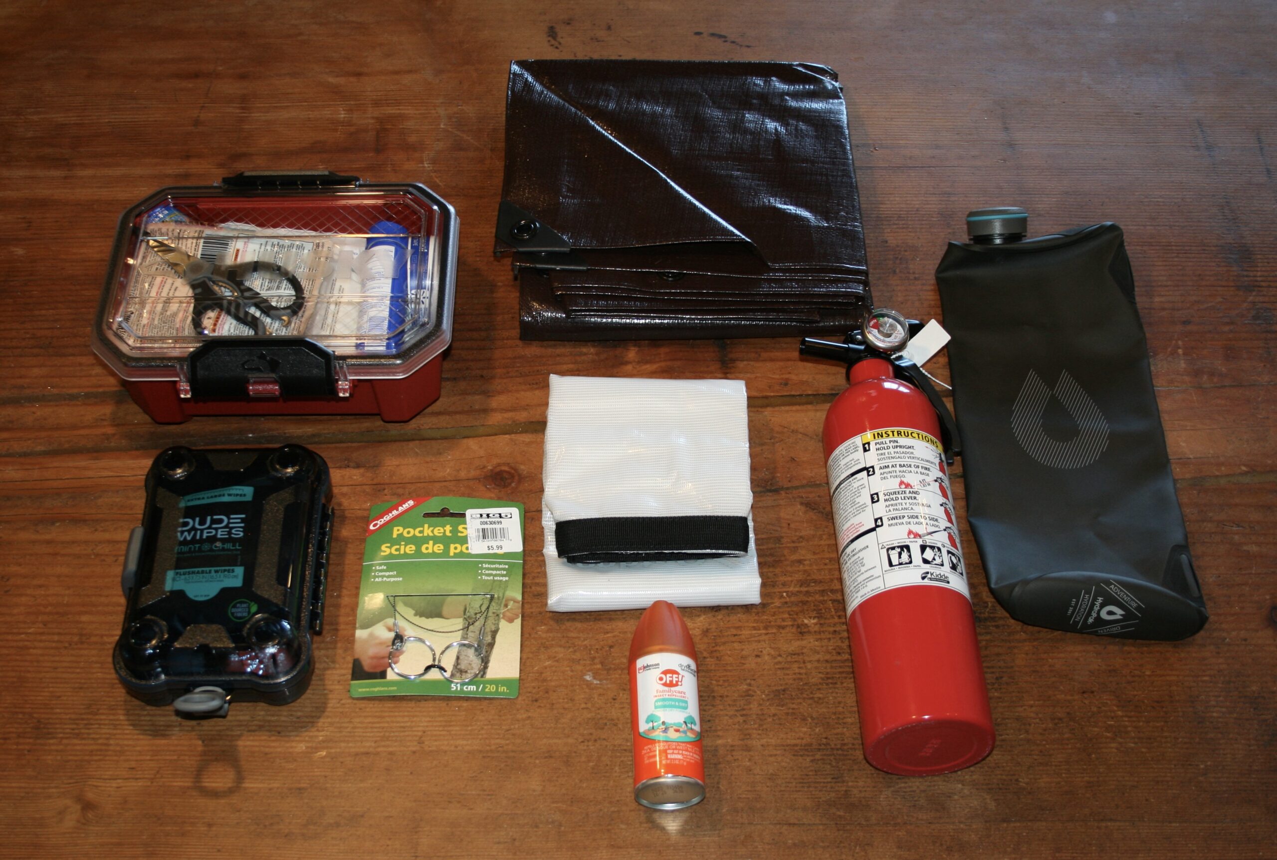 Tacoma TRD Pro driver side behind seat gear flatlay showing first aid case, tarp, fire extinguisher, and dry bag