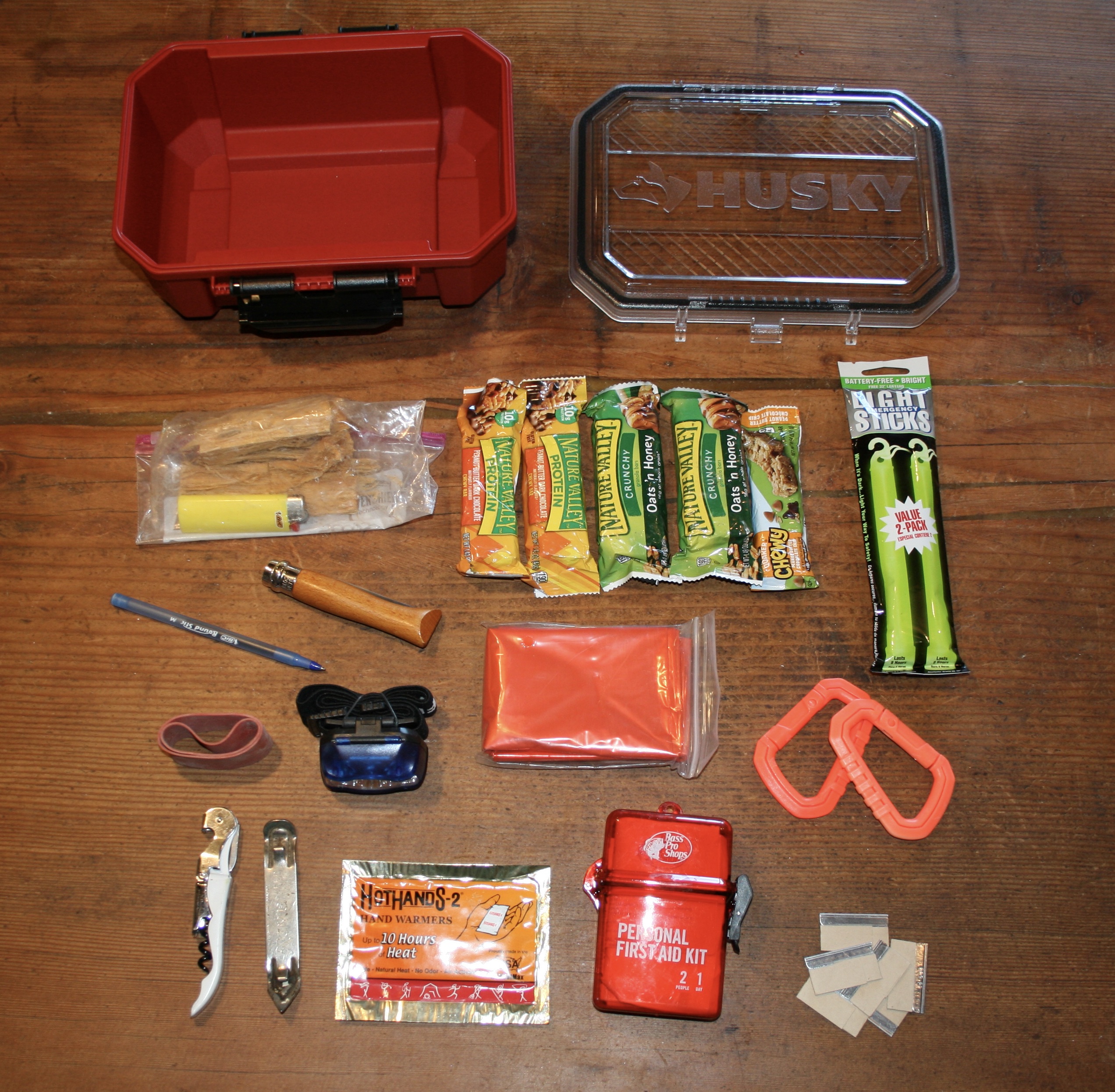Zone 7 supplies flatlay showing Nature Valley bars, ferro rod, waterproof lighter cases, tinder, recovery strap, and Husky snack case on wooden surface
