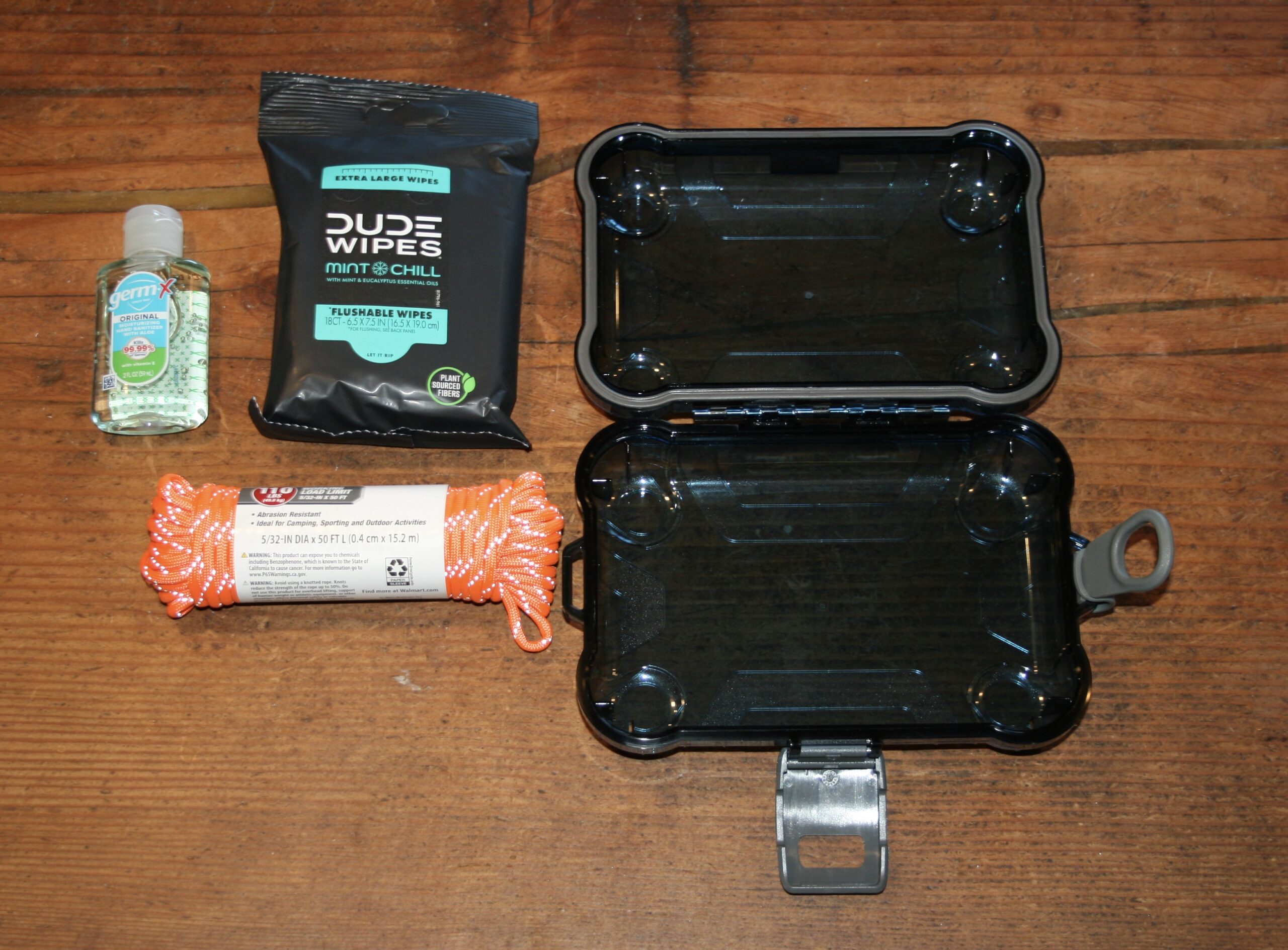 Watertight case open beside hand sanitizer, Dude Wipes, and paracord
